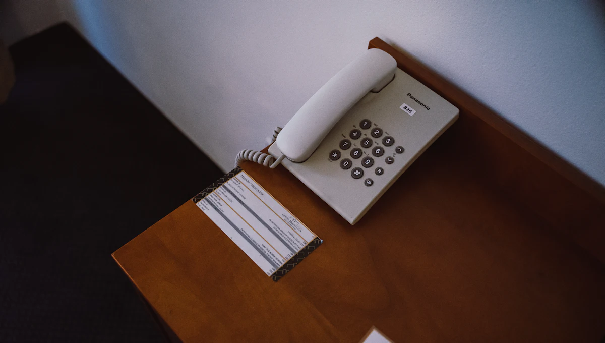 A room telephone on a bedside desk, the room number on the handset and the hotel's dialling card beside it.