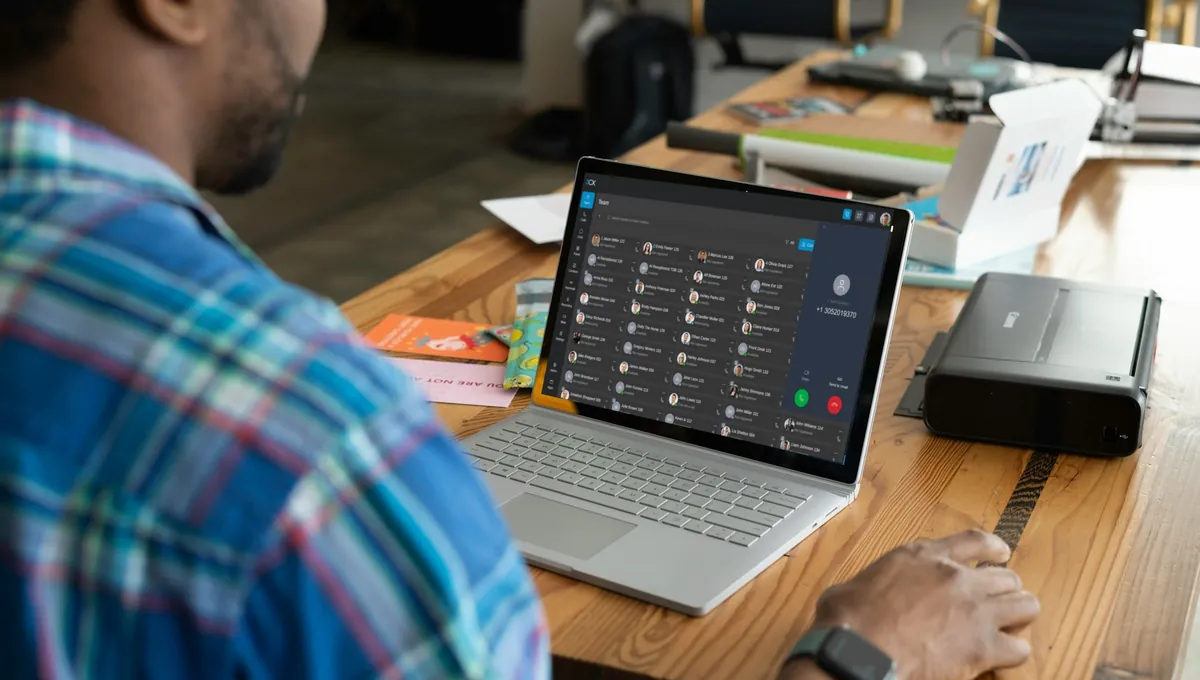 A man at a desk with the 3CX Web Client open on his laptop, an incoming call showing beside his team.